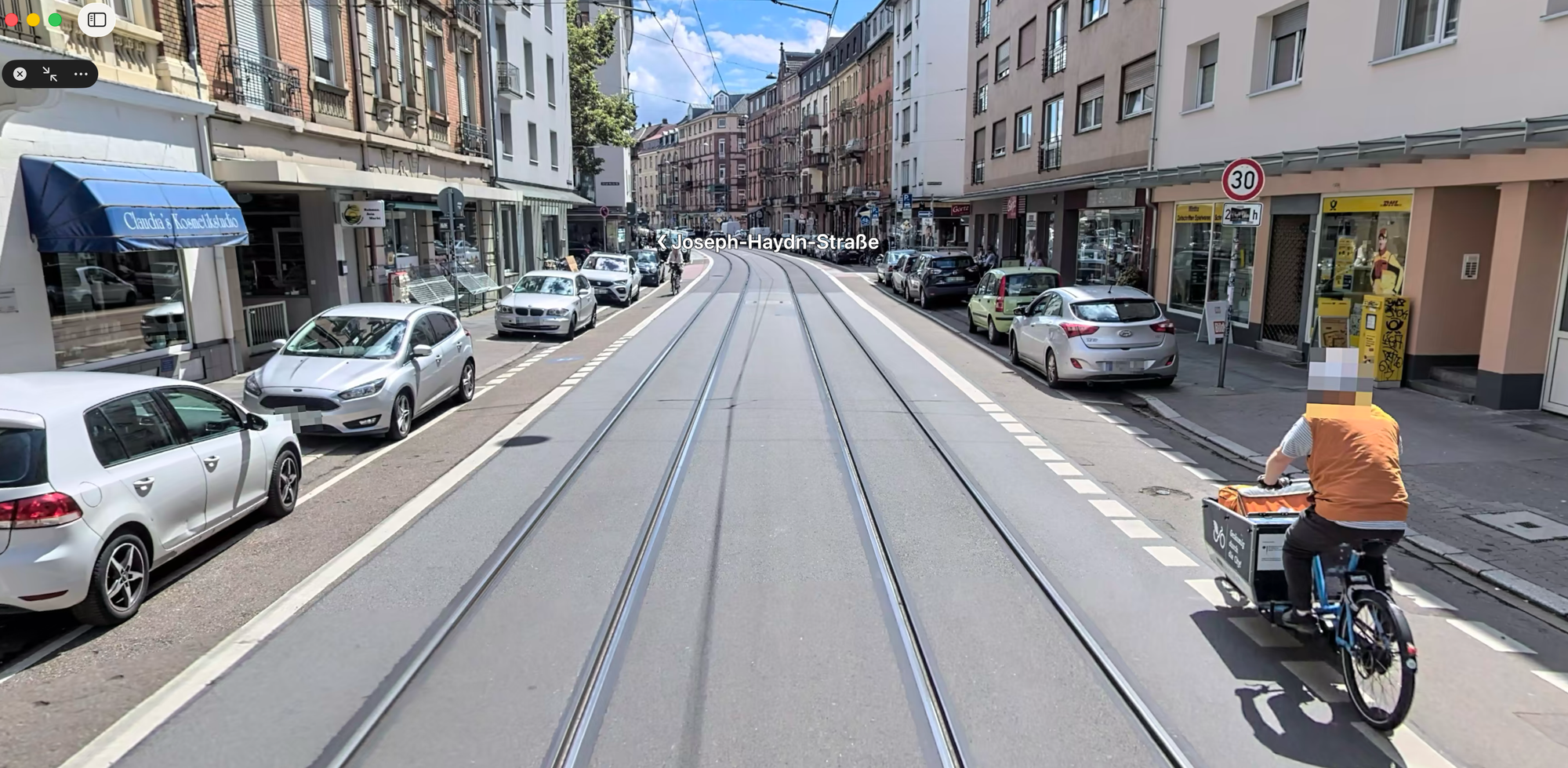 Querschnittsaufnahme der Seckenheimer Straße auf Höhe der Post mit einem Lastenradfahrenden der sich an den linken Radwegrand orientiert, da der Radweg für ihn nicht sicher nutzbar ist, ohne Dooring-Gefahr.