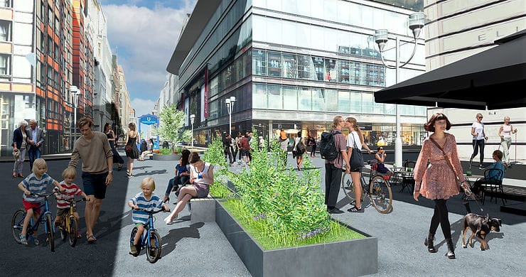 Die Friedrichstraße als Fussgängerzone. Eine lebhafte Straßenszene mit Kindern auf Fahrrädern, einer Frau mit Hund, begrüntes Stadtmobiliar und Sitzgelegenheiten laden zum verweilen ein.