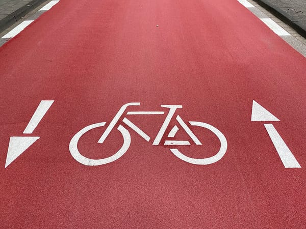 Zweirichtungsradweg, rotmarkierte Fahrbahn, mit weiß aufgemaltem Rad und Pfeilen die in beide Richtungen zeigen